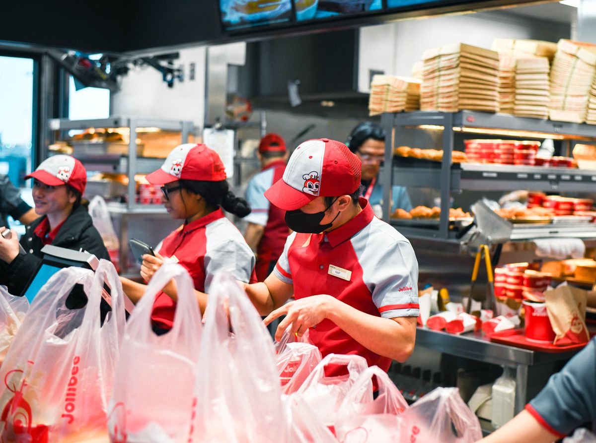 Jollibee employees in red and gray pack plastic to-go bags.