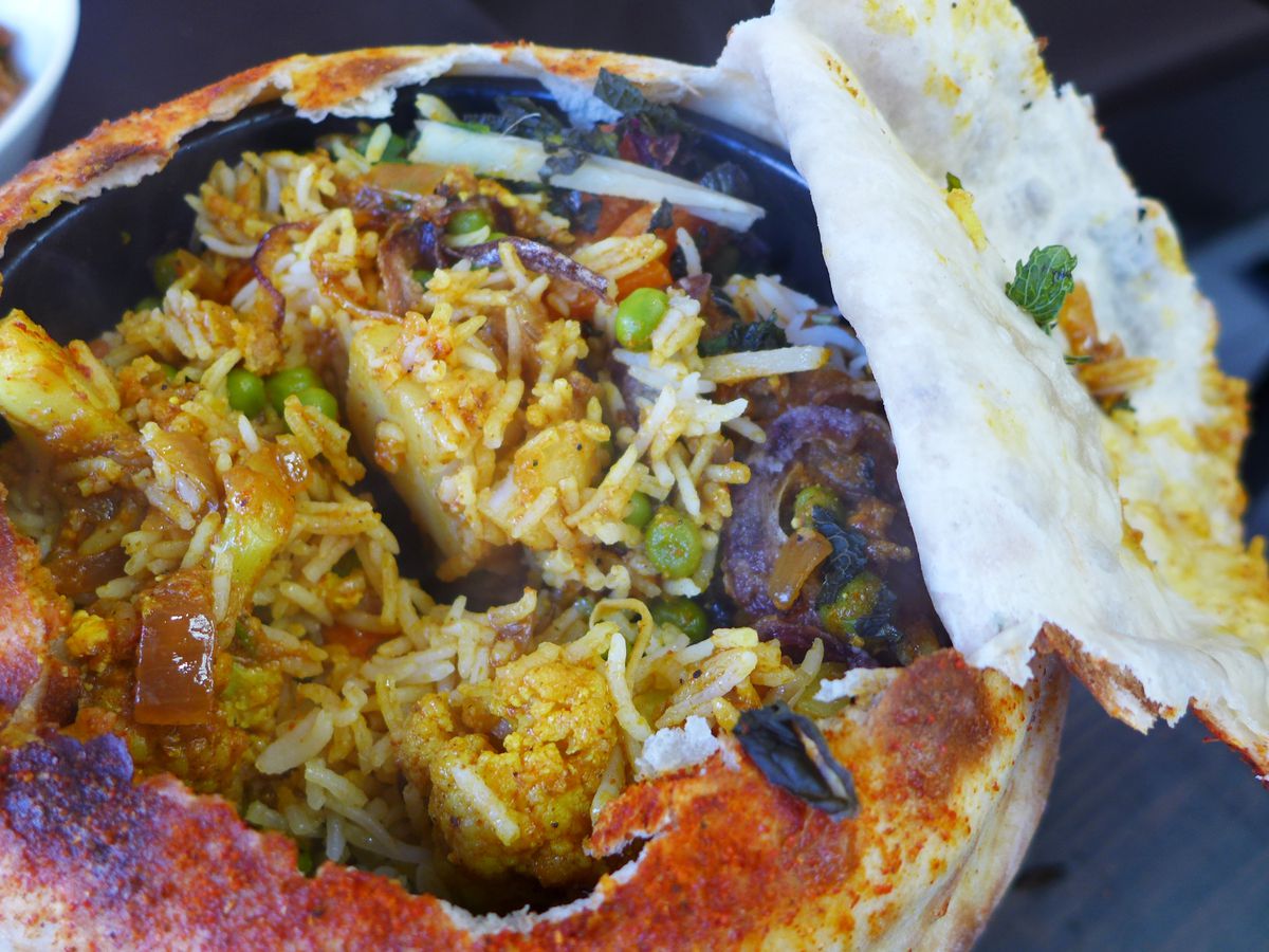 A vegetarian biryani pie with the crust on top torn open to reveal the filling.