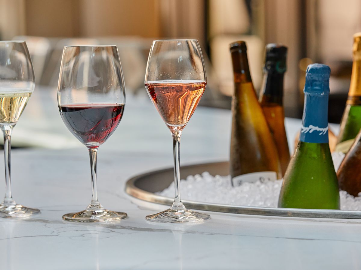 Three glasses of wine (a white, rose, and red) sit on a white bar top next to an ice bath of wine bottles.