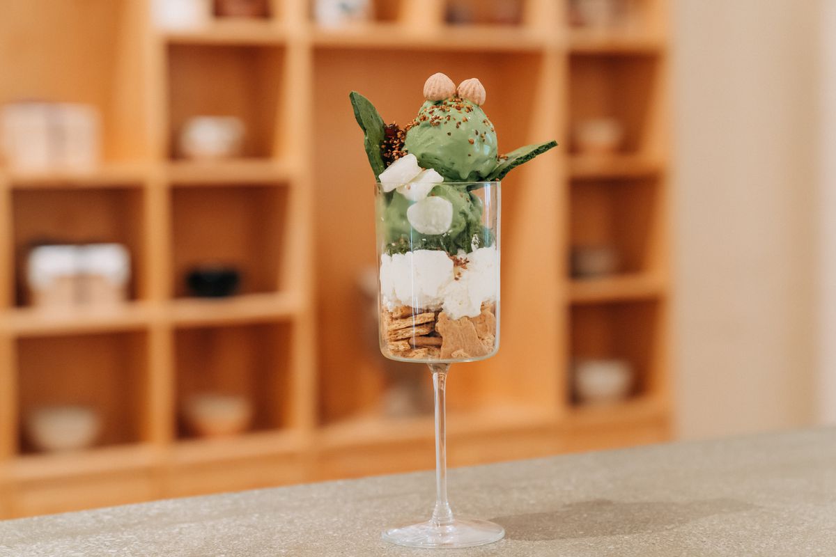 A clear, stemmed glass filled with crushed graham crackers, whipped cream, and green matcha gelato.