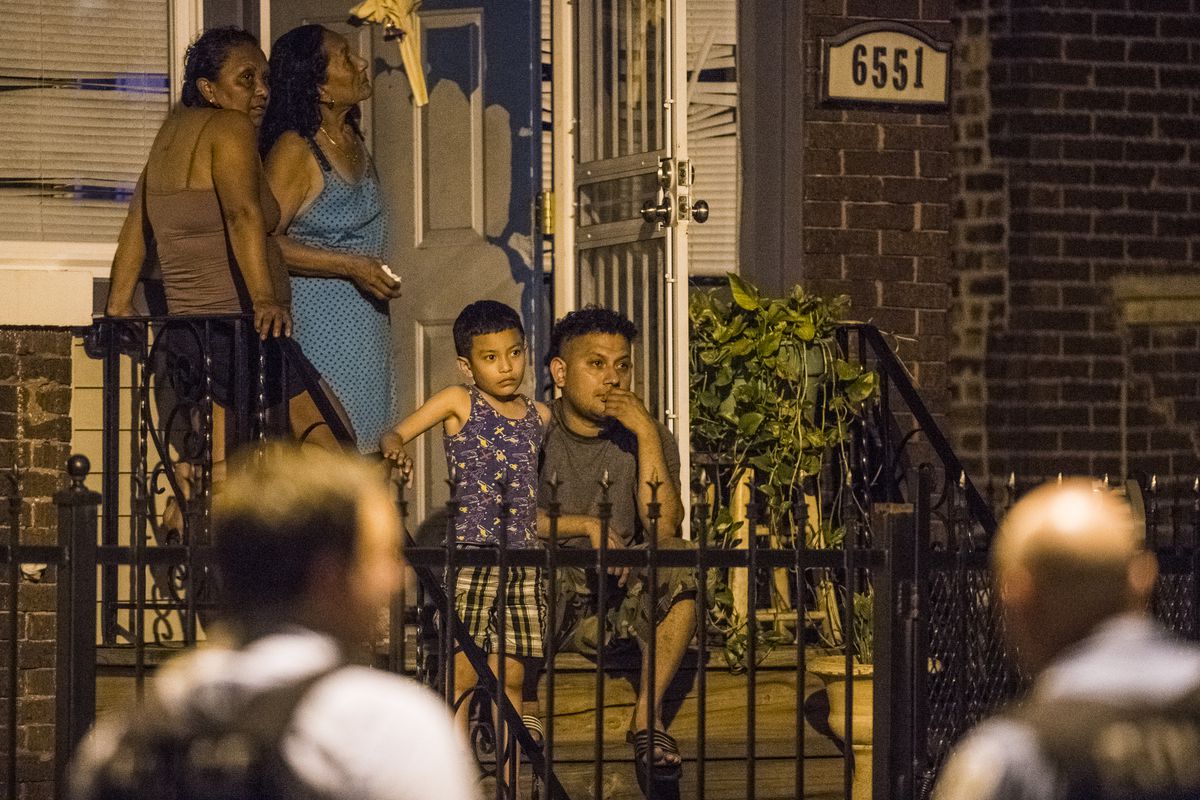 A family sits on their porch as police investigate the scene of a person shot and killed Sunday night in the 6500 block of South Maplewood in Chicago. The person was shot and killed in front of this families home. | Tyler LaRiviere/Sun-Times