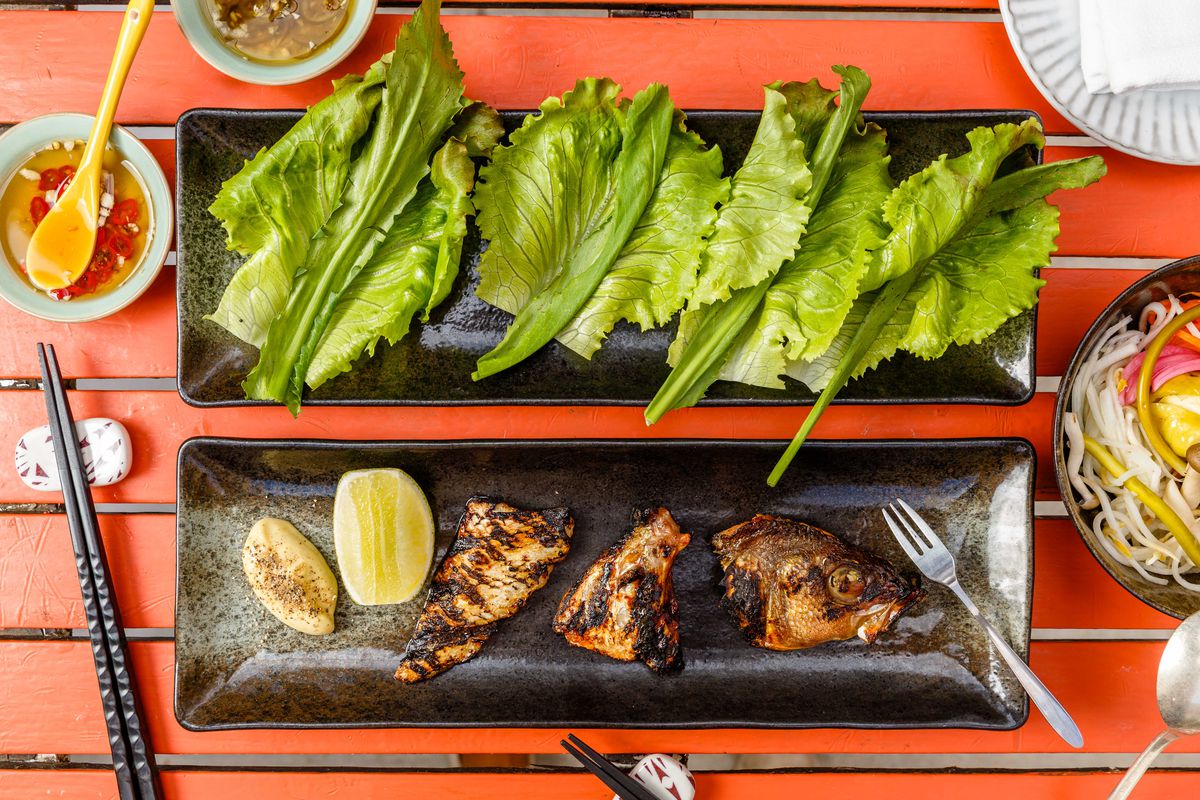 Fish head, collar, and belly sits on a plate next to a separate dish of lettuce leaves
