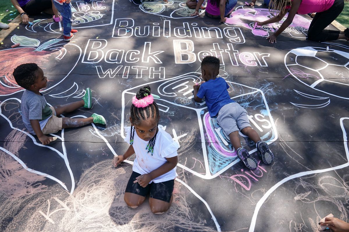 Children draw a chalk mural on a blacktop playground surface.