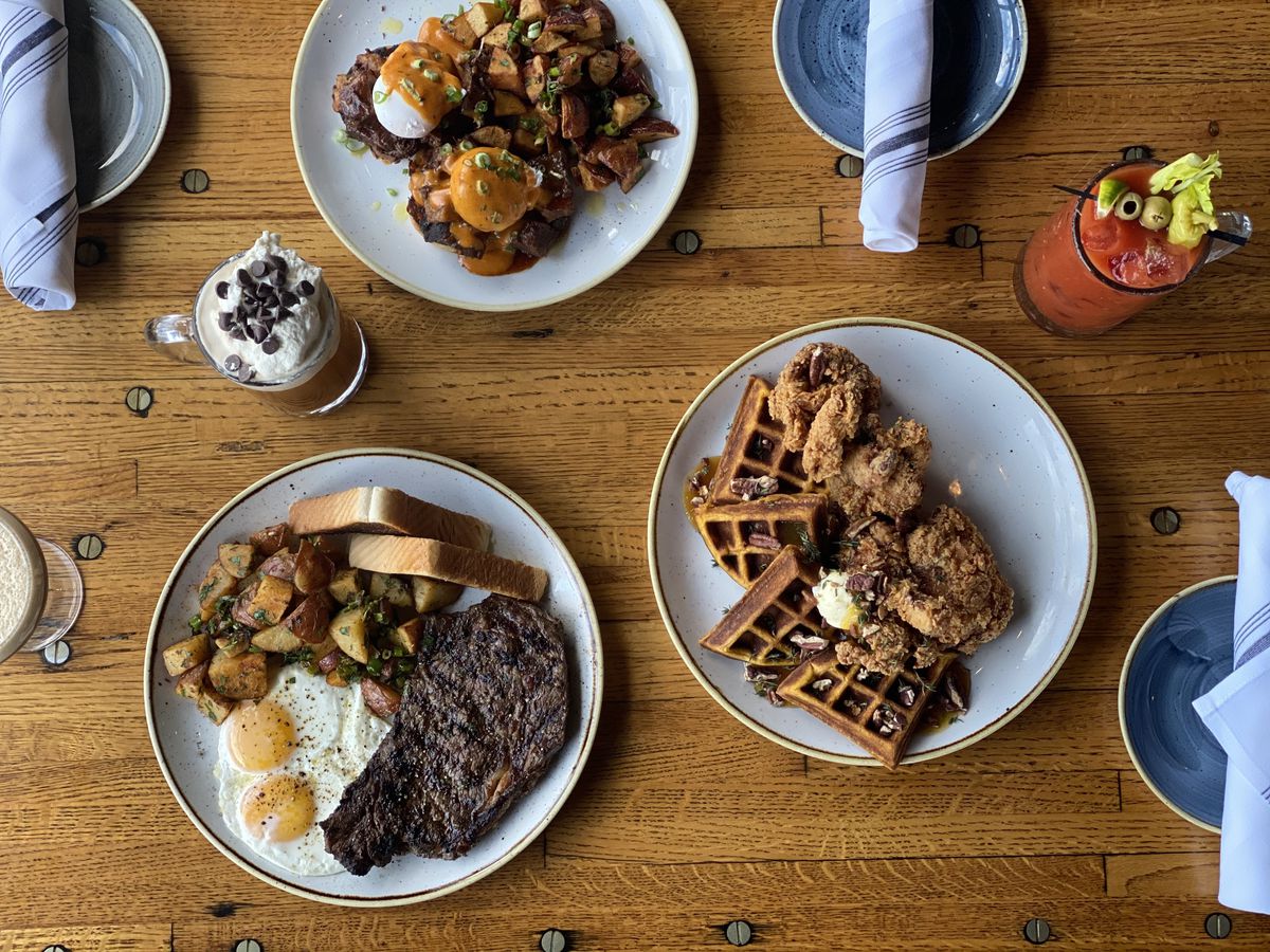 Overhead view of a wooden table covered with several dishes of brunch food and cocktails
