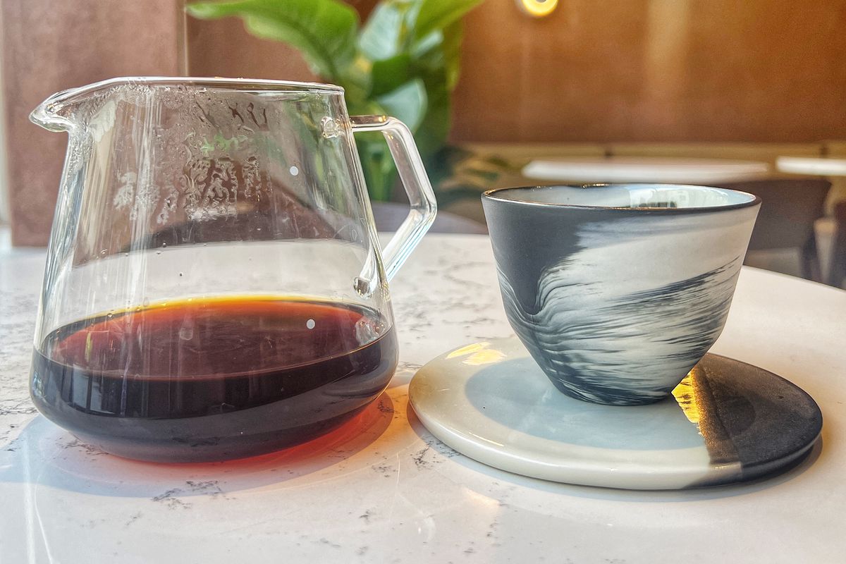 Filter coffee in a glass jug, next to an ornately glazed ceramic cup.