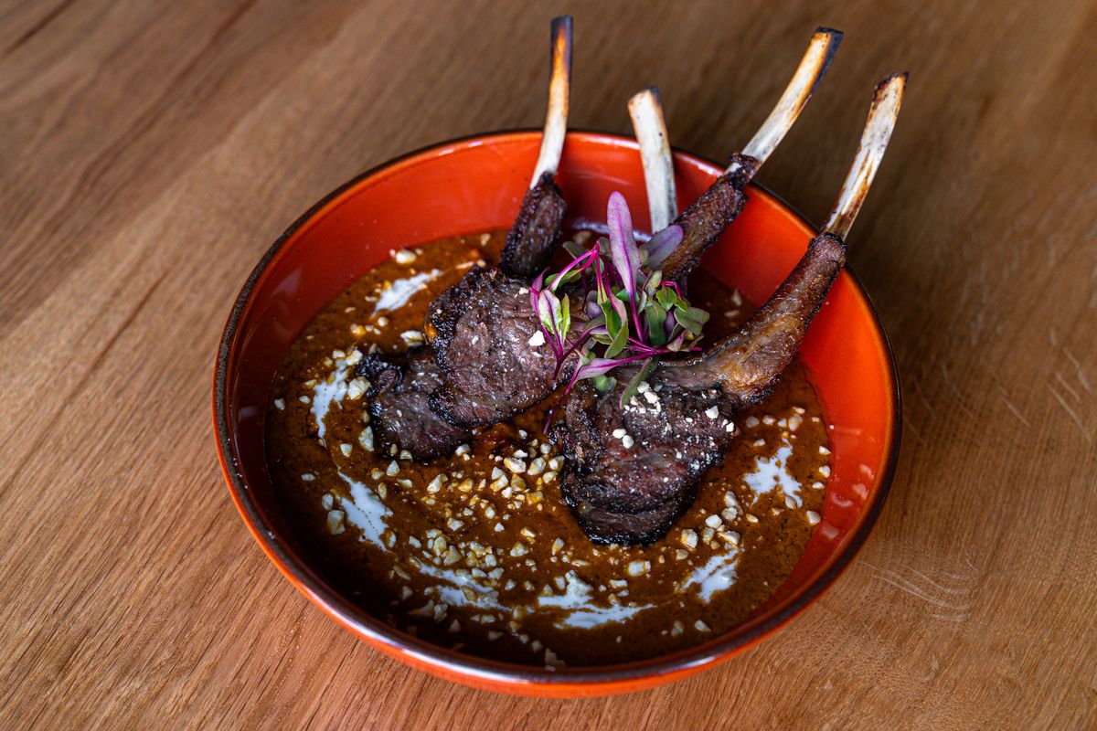 A red bowl holds four grilled lamb chops in dark sauce.