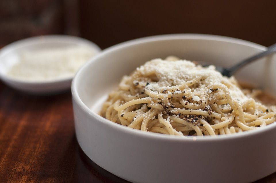 A bowl of noodles covered in grated parmesan and black pepper.
