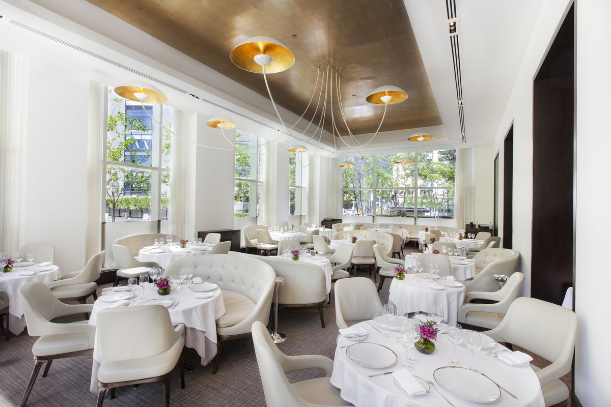 The Jean-Georges dining room, with plush cream chairs set at tables with white tablecloths