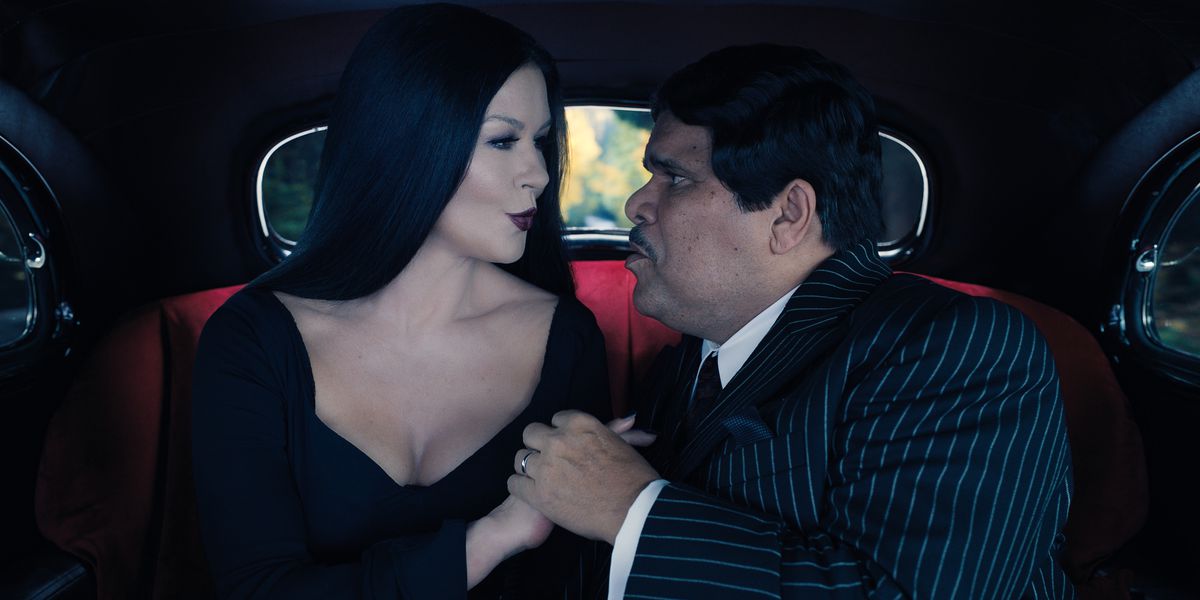 Morticia și Gomez se sărută în spatele unei mașini.  amândoi sunt îmbrăcați în negru și se privesc cu adorație unul în ochi