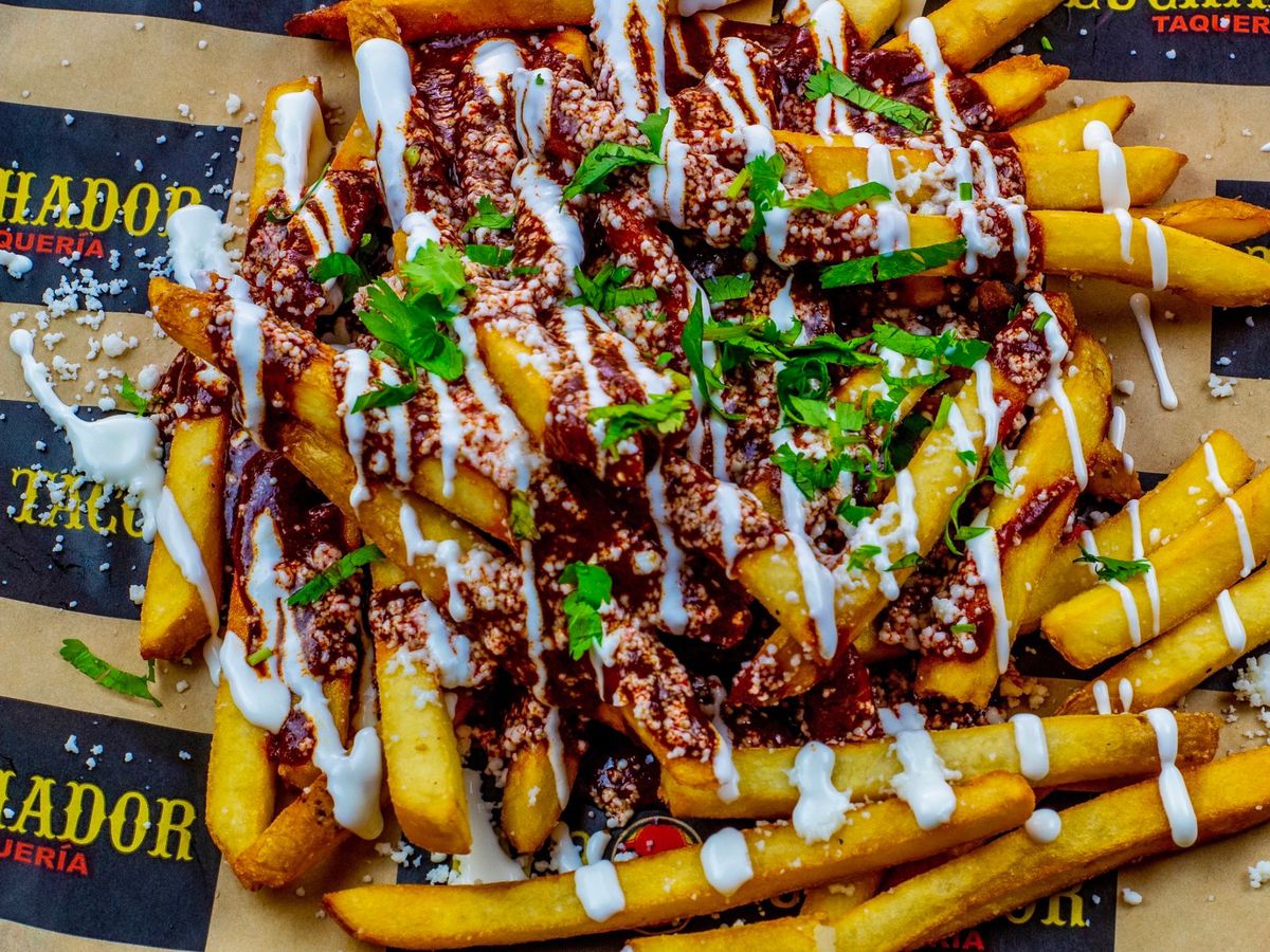 A pile of fries topped with mole and diced herbs on branded wax paper