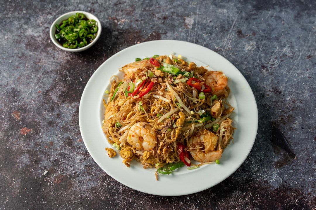 A plate of Malaysian prawn noodles with spring onions, on a stone background