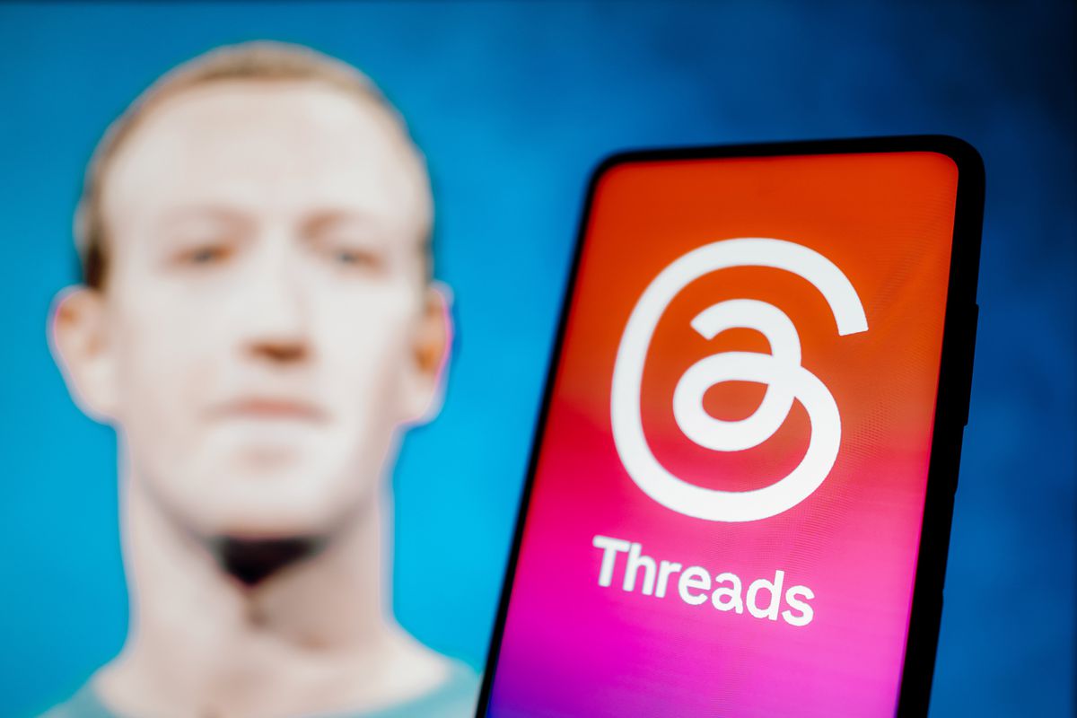 In this photo illustration, the Threads logo is displayed on a smartphone screen with the image of Meta CEO Mark Zuckerberg in the background.&nbsp;