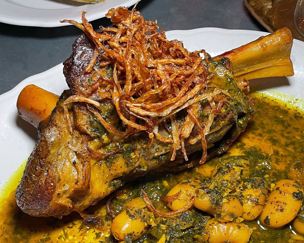 A lamb shank on the bone, topped with crispy fried onions and set in a bowl of yellow sauce with herbs and butter beans.