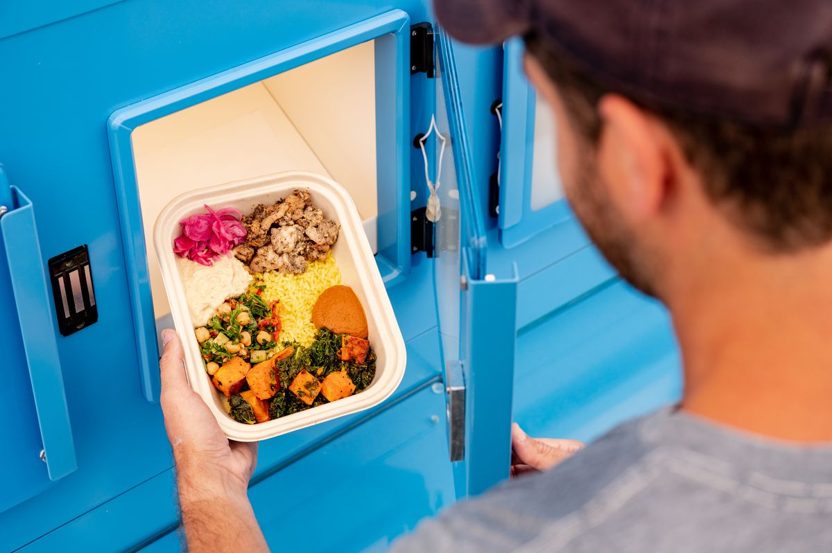 A customer takes a grain bowl out of a locker on the side of the Mezli box.