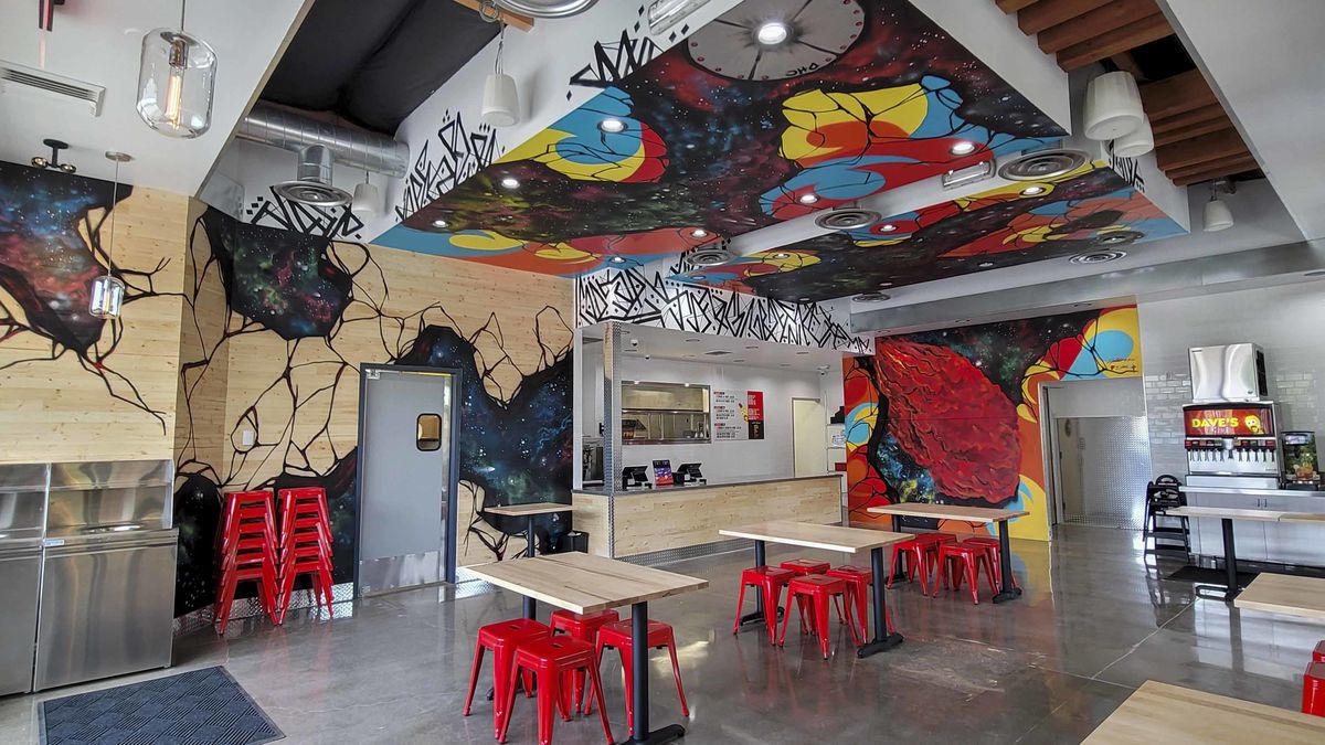 Walls of the Dave’s Hot Chicken location in Tualatin include colorful murals, as if the wood is peeling away to reveal red, blue, and yellow bursts. The interior space also includes a number of tables and red stools, with a walk-up counter.