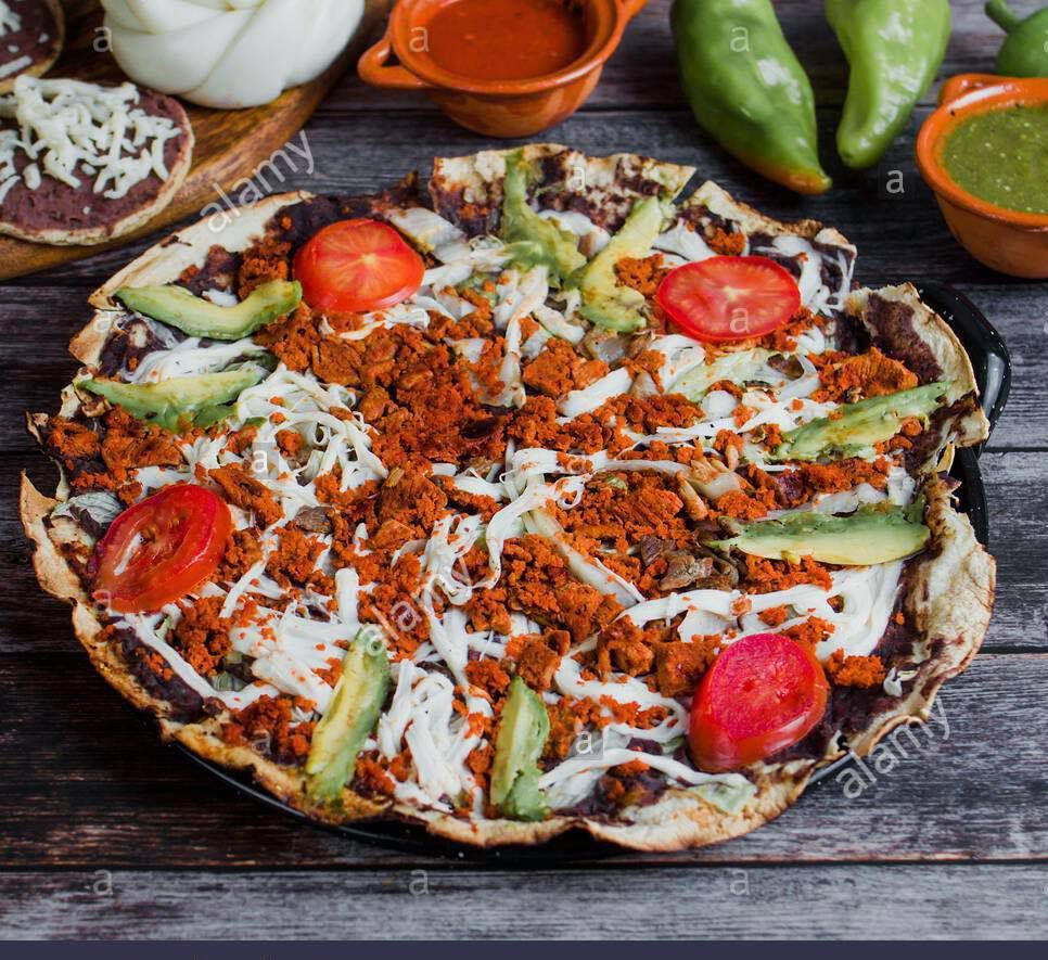 A large chorizo-topped tlayuda with slices of tomato, avocado, and cheese