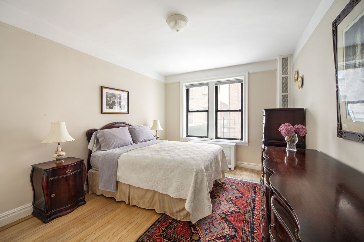 A bedroom with hardwood floors, a medium-sized bed, two windows, and wooden furniture.