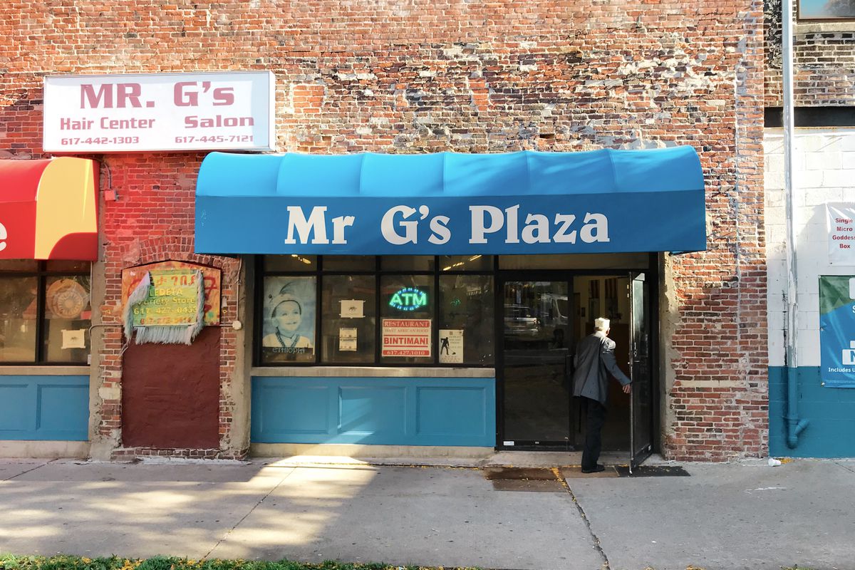 A brick building with a blue awning that reads “Mr. G’s Plaza” in white font.