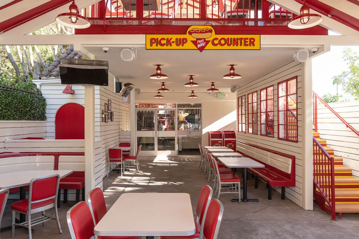 A shaded red and white retro hot dog restaurant at daytime.