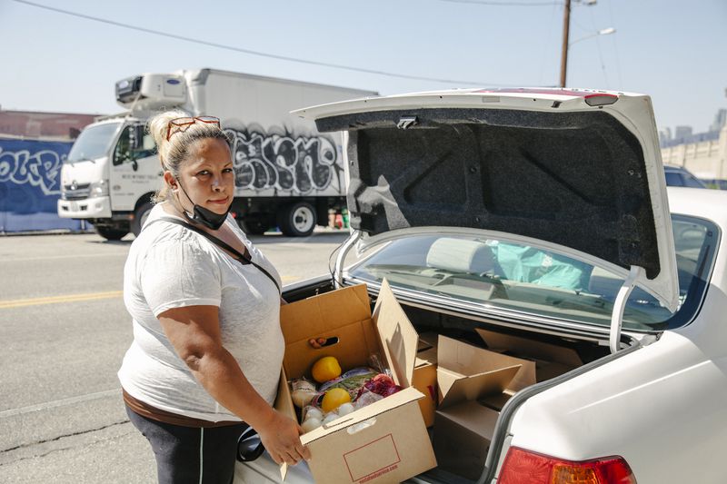 Woman carries a box containing food into the trunk of a car.