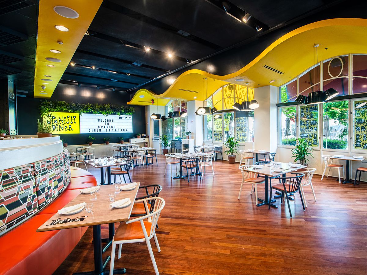 A restaurant dining room with colorful banquettes, yellow ceilings and a marquee-style menu.
