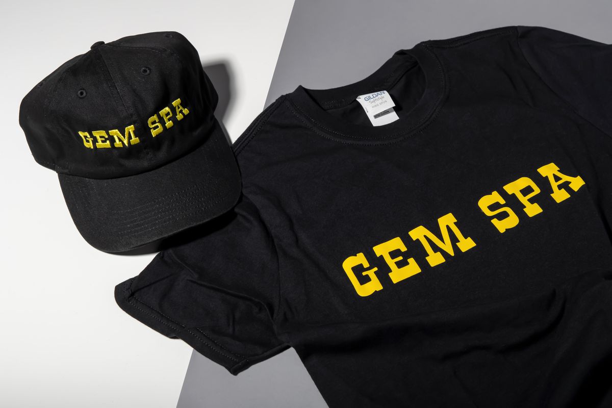 A black hat and black t-shirt that say “Gem Spa” in yellow writing