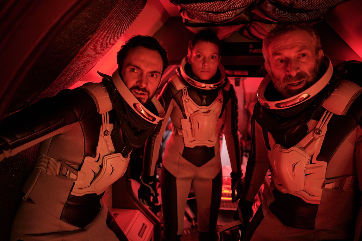 Gavin Abbott, Hannah Wagner and Dimitri Krylow look concerned in space suits with red lighting in Rubikon
