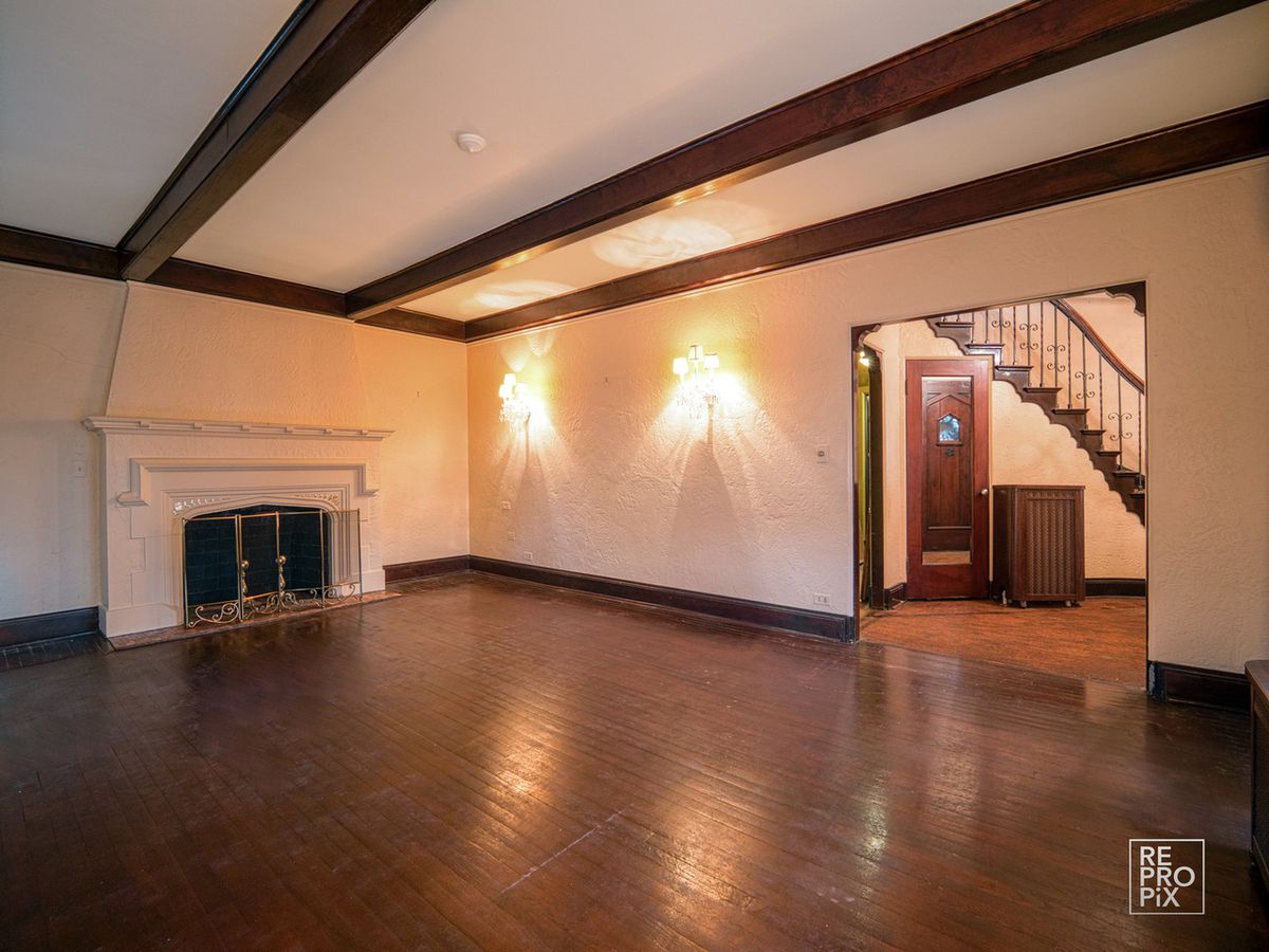 A living room with sconce lighting, wooden beams, and a large white mantle fireplace.
