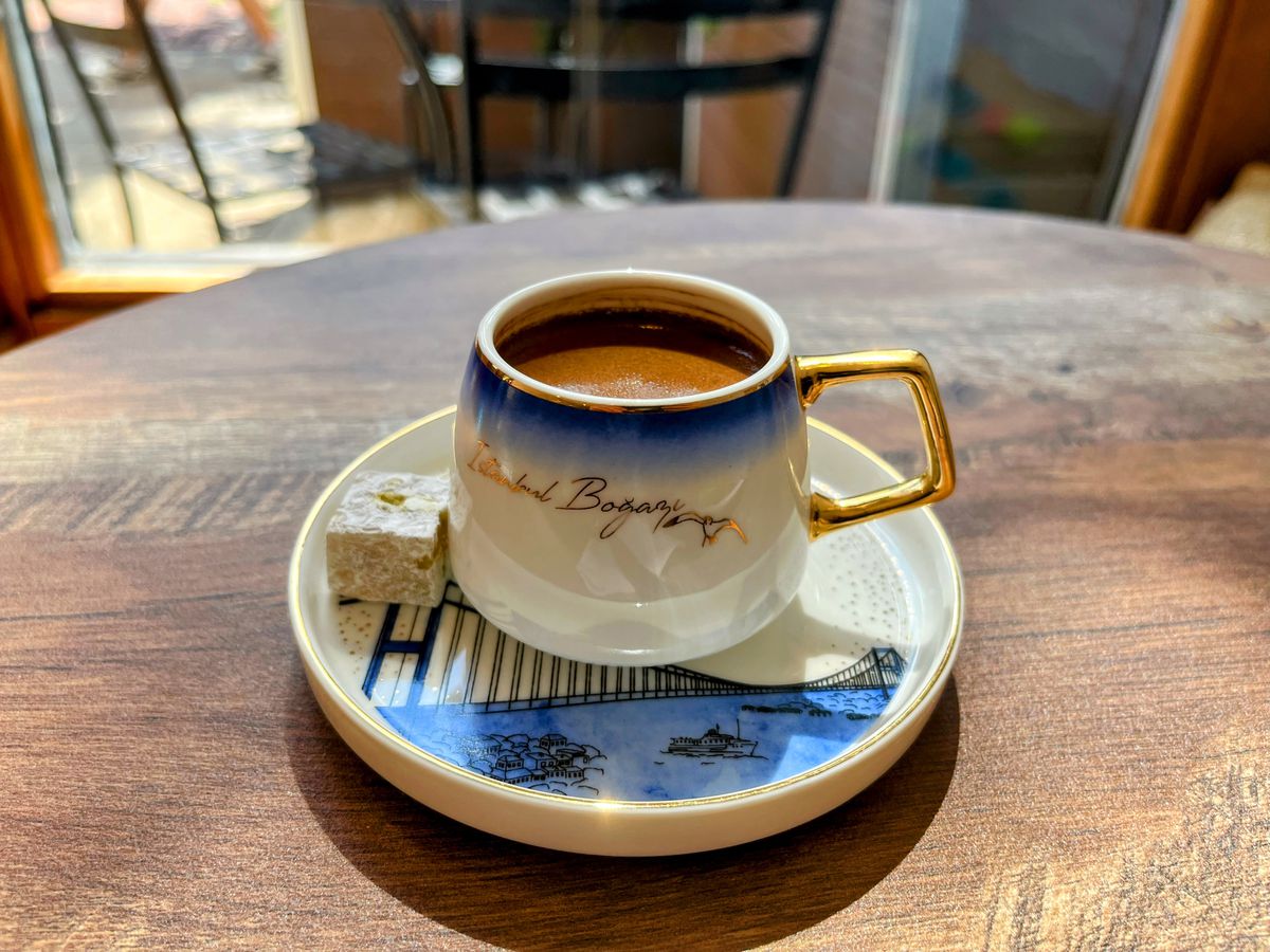 A blue and white espresso-sized coffee cup with gilded gold edges and chocolate-hued coffee inside.