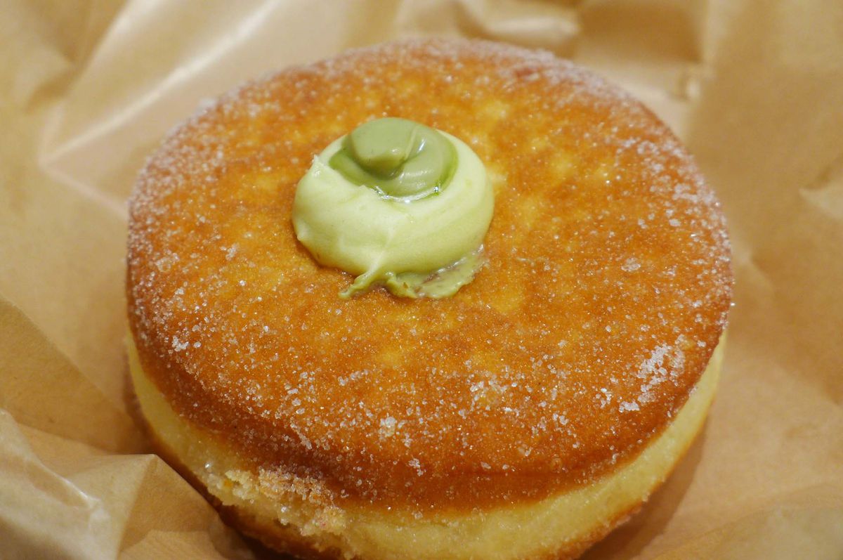 A round donut with green custard oozing out a hole in the top.