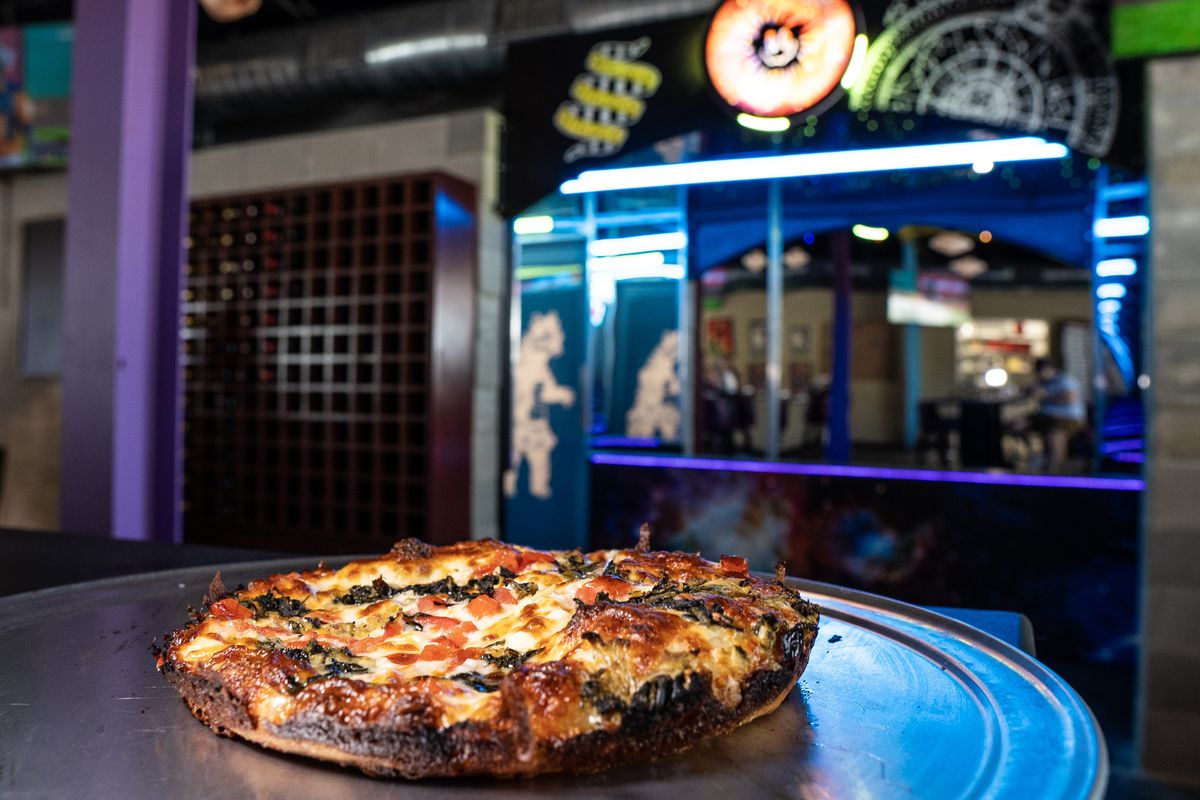 A spinach artichoke pizza in front of the neon-lit bar at Betelgeuse Betelgeuse.