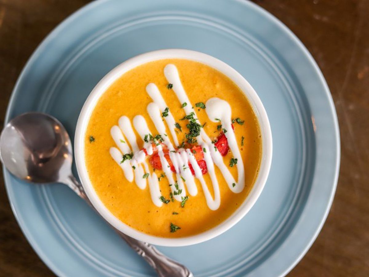 A bowl of orange-yellow soup with a drizzle of white sauce.