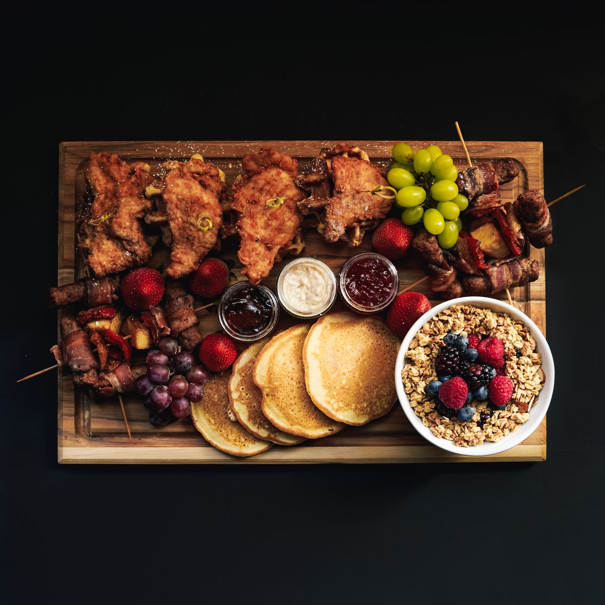 A brunch board&nbsp;with pancakes, fried chicken, bacon, and fresh fruit. 