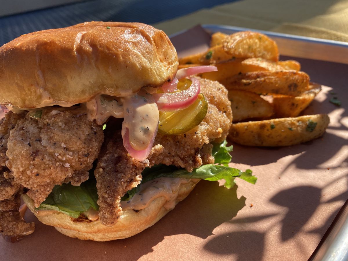 Fried chicken sandwich with pickles, pickled onions, and lettuce and a side of herbed potato wedges