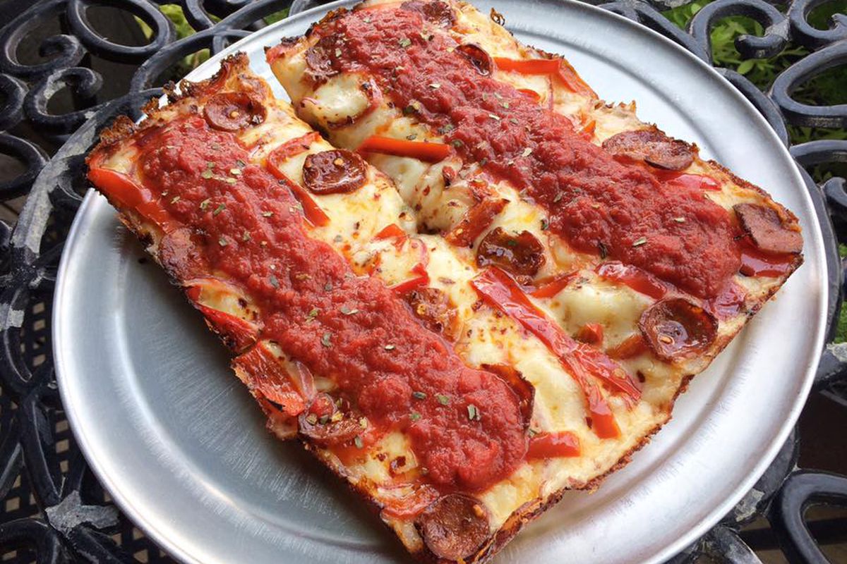 A rectangular pie of thick cheese pizza topped with sauce and sausages on a round metal tray