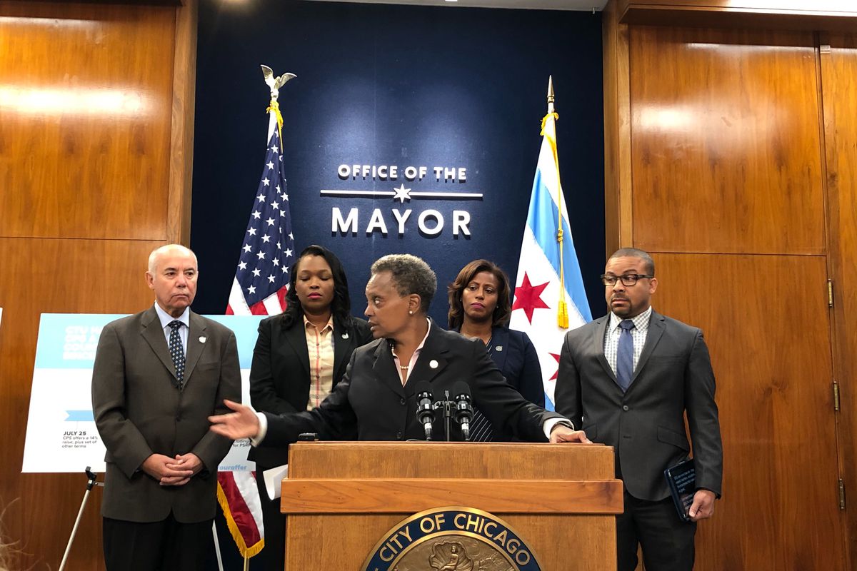 Chicago Mayor Lori Lightfoot stands at a wood podium. Four of her colleagues are behind her as are a U.S. flag and a city of Chicago flag.