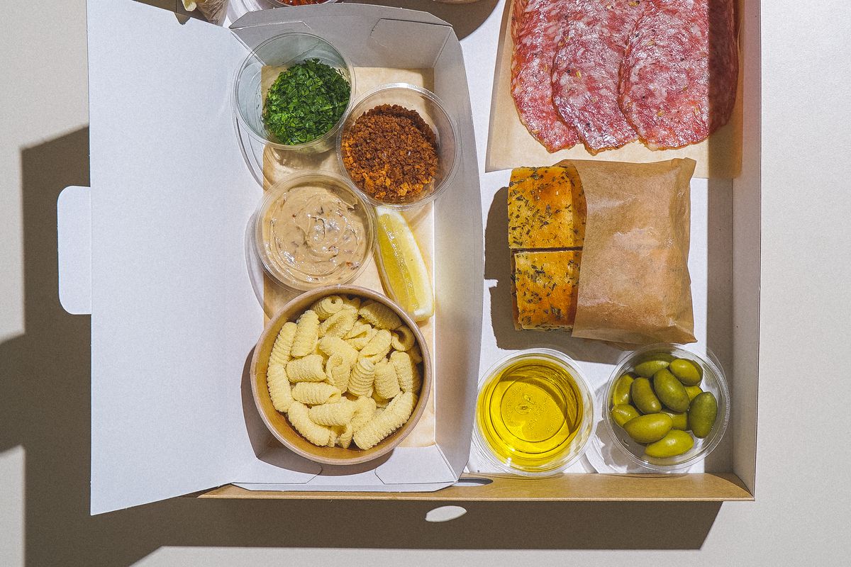 Fresh pasta, sauce, salumi, foccaccia, and olives in a cardboard meal kit box, shot from a birdseye view