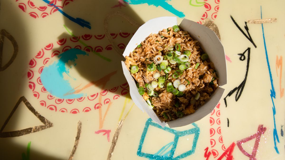 An overhead shot of a takeout counter with fried rice and scallions on a colorful yellow, red, and blue background.