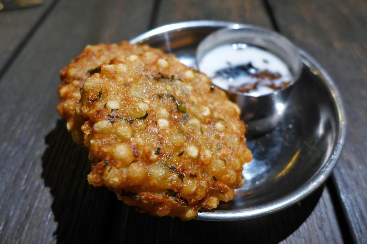 A brown fritter with a small cup of yogurt sauce in the background.