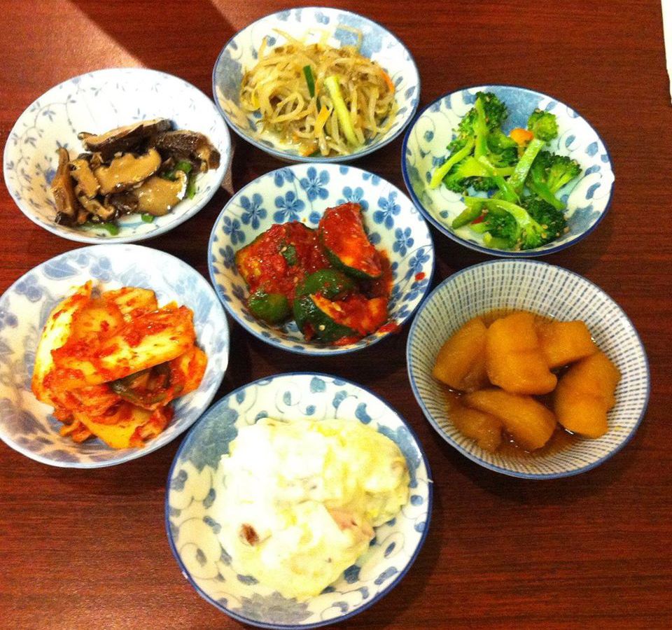 assorted banchan in scattered bowls, on red surface