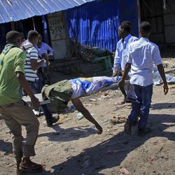 Somali men retrieve the body of a victim killed when a car bomb targeted a police station in the Waberi neighborhood, where President Hassan Sheikh Mohamud was visiting a university, in the capital Mogadishu, Somalia Saturday, Nov. 26, 2016. A Somali police official says a car bomb has exploded near a police station in a busy market in the Somali capital, killing a number of people and wounding others. 