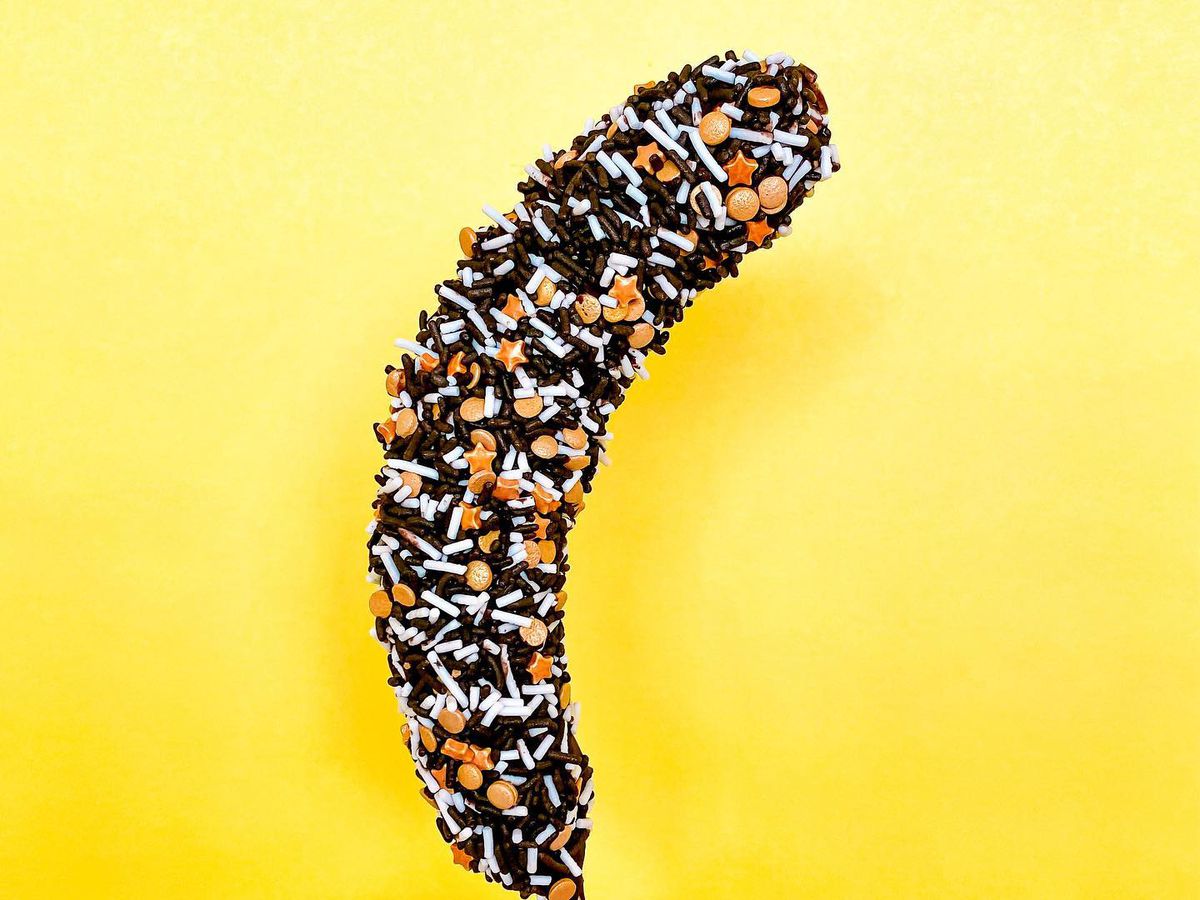 A hand holds a frozen chocolate banana on a yellow background.
