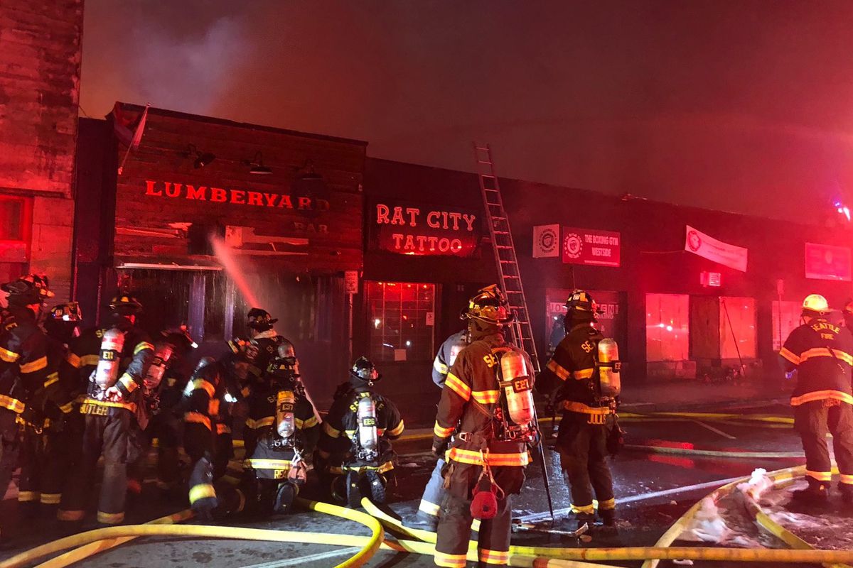 Firefighters work to control a blaze at night in fron of the Lumber Yard Bar and Rat City Tattoo in White Center