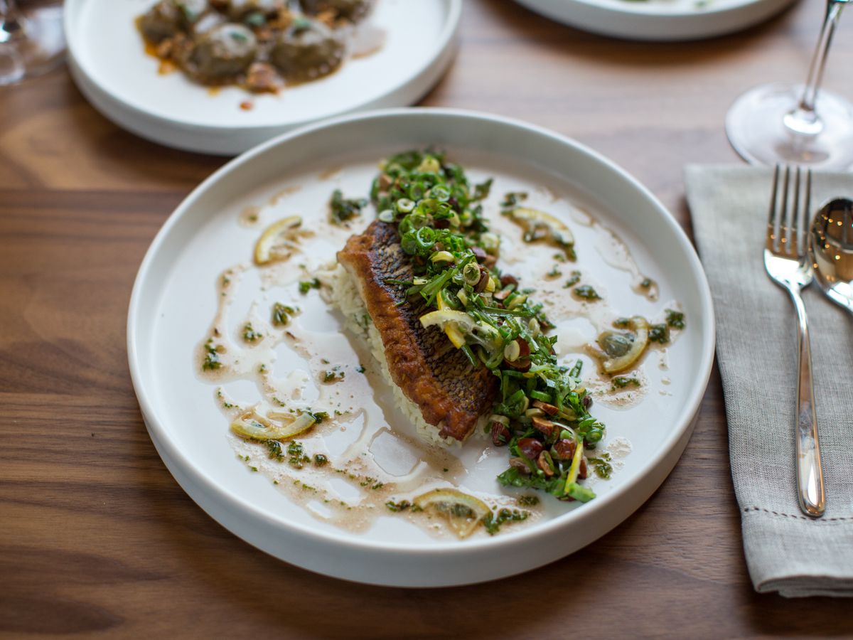 Grilled trout, cauliflower, toasted almond, green grape, and basmati rice on a white dish with fork and spoon over a gray napkin.