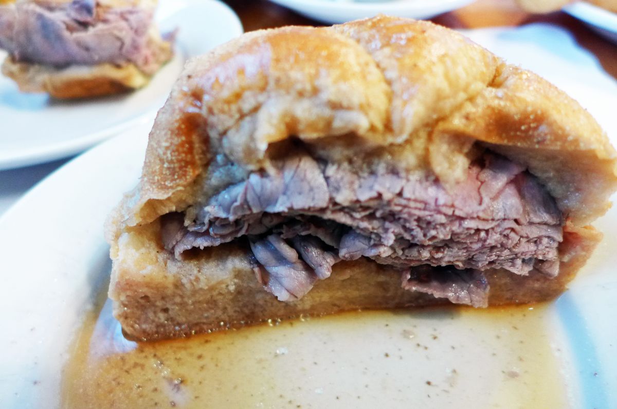 A roast beef sandwich drenched with beef broth on a plate is photographed in a cross section.