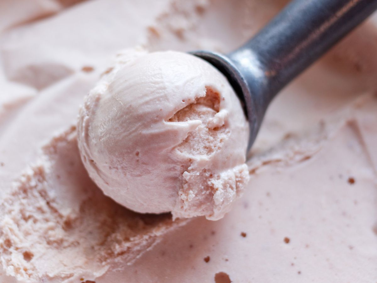 A closeup of a ball of strawberry ice cream in an ice cream scoop atop more strawberry ice cream.