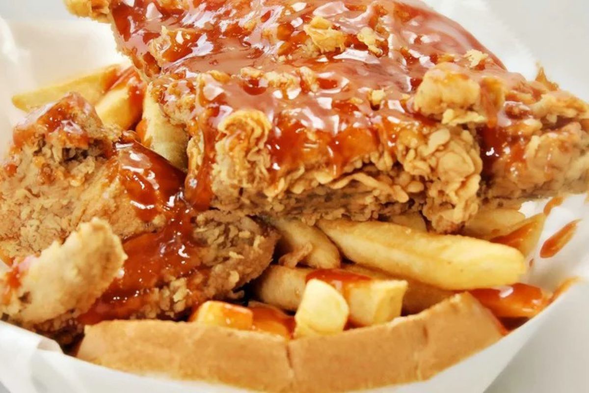 A plate of fried chicken and french fries smothered in sauce.