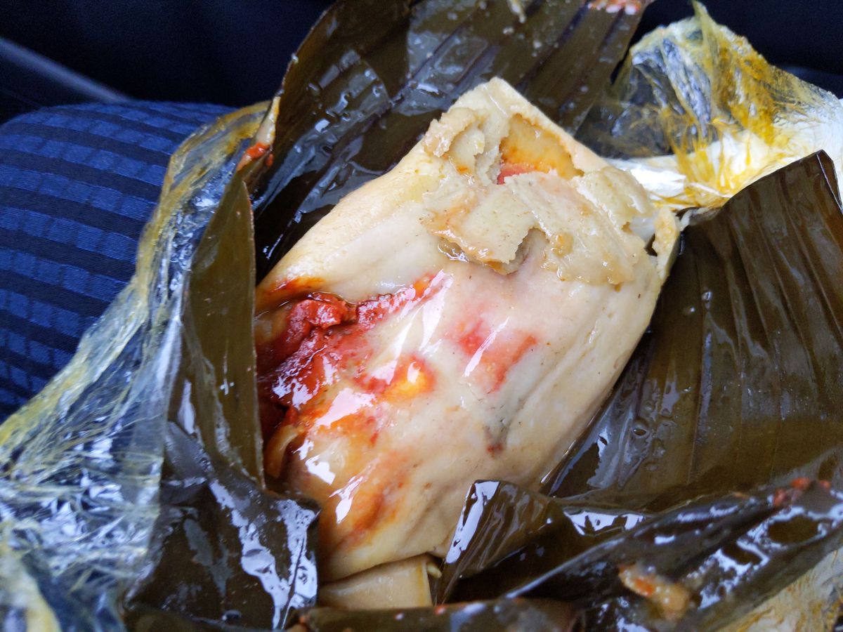 A glistening tamale with bright red veins emerging from a dark green banana leaf wrapper. 