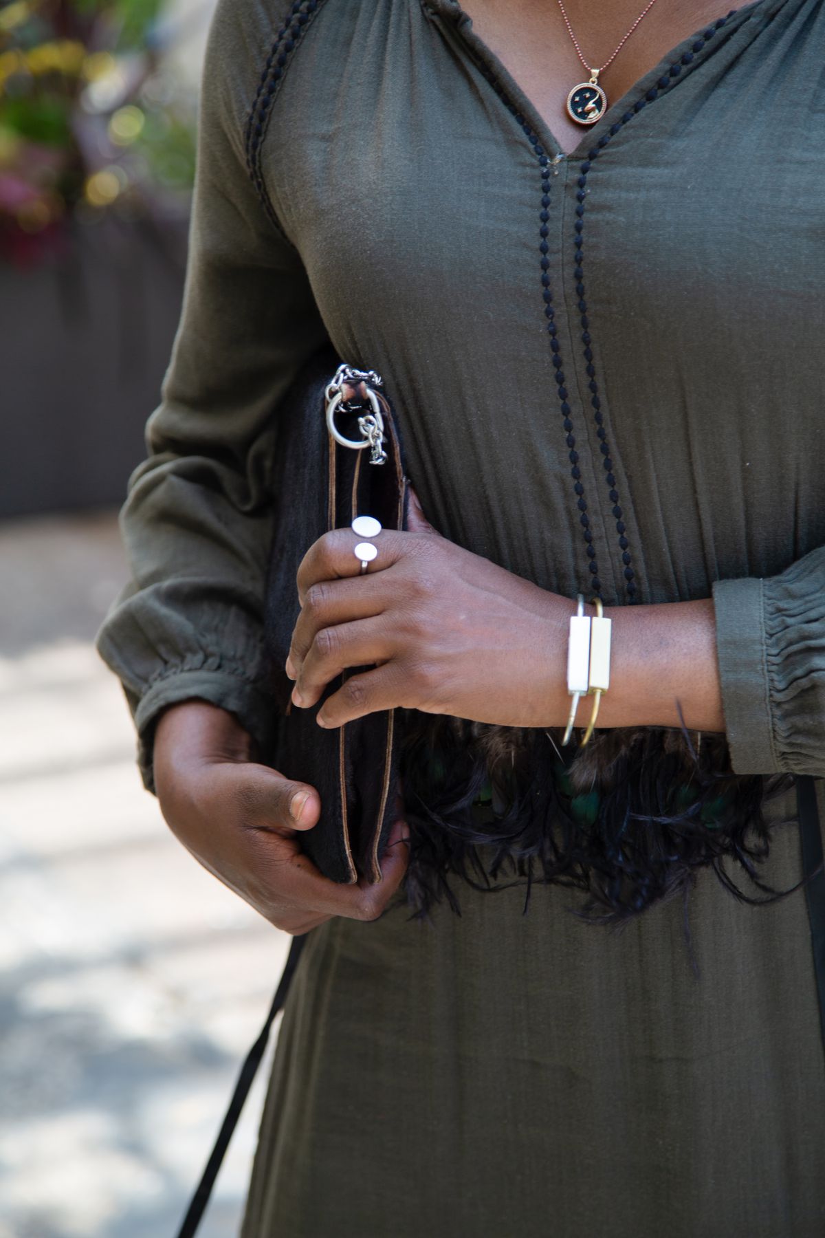 A woman holds a leather clutch and shows off her rings and two bracelets.