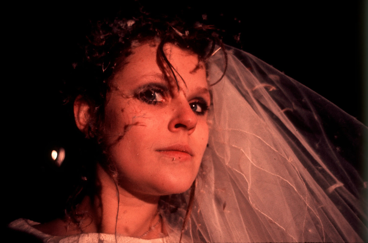 A woman wearing a wedding veil with dirt on her face looks at the camera in The Other Side of the Underneath.